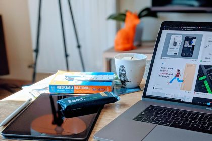 macbook pro beside white ceramic mug on brown wooden table