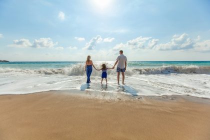 man, woman and child holding hands on seashore