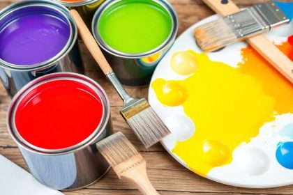 Colorful paint cans and brushes on a wooden table.