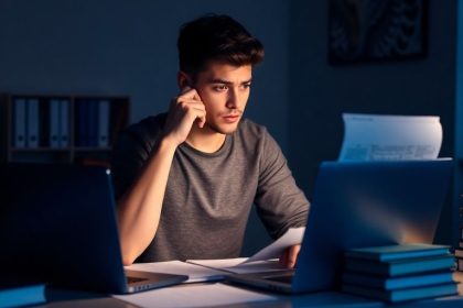 Student studying with books and laptop at desk.