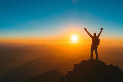 Hiker celebrating success at a mountain summit during sunrise.