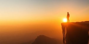 Person at cliff edge, sunset creating a motivational scene.