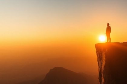 Person at cliff edge, sunset creating a motivational scene.